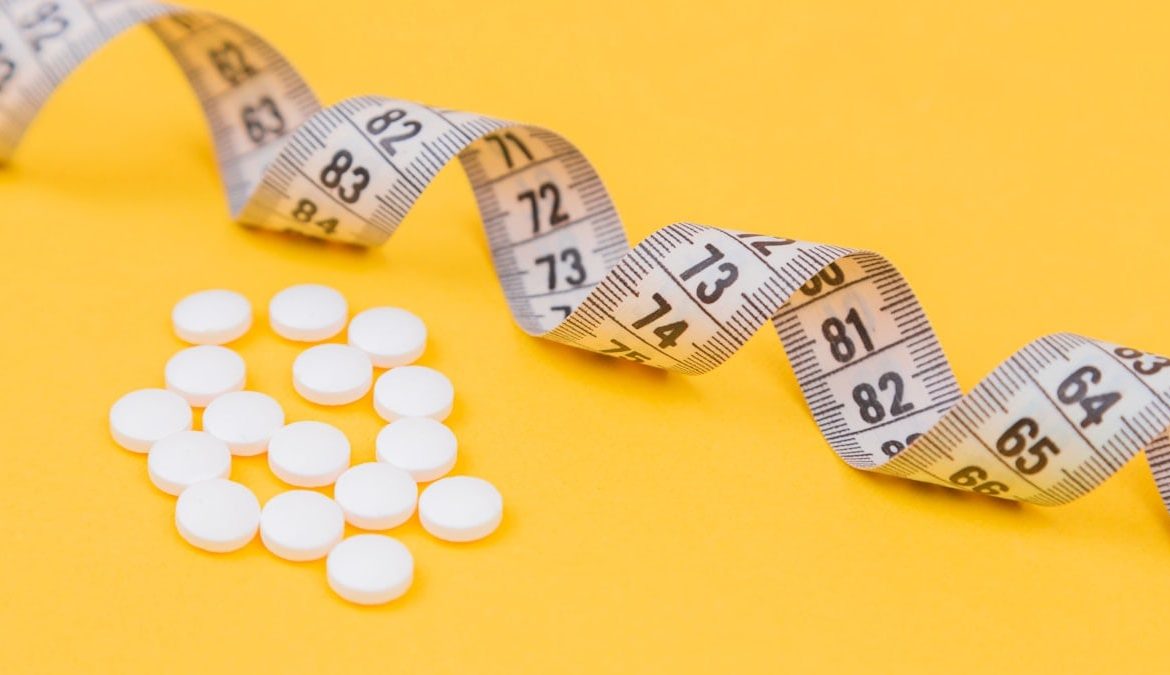 White measuring tape with a white pills, white vitamin on a yellow background. Diet. Slimming. Obesity. Place for an inscription. Weight loss marathon. Advertising. Top view. The close plan.